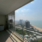 Balcony with glass railing overlooking a sandy beach, blue sea, and city high-rises in the distance (oceanfront view)