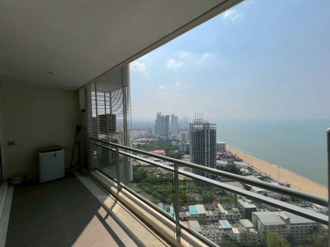 Balcony with glass railing overlooking a sandy beach, blue sea, and city high-rises in the distance (oceanfront view)