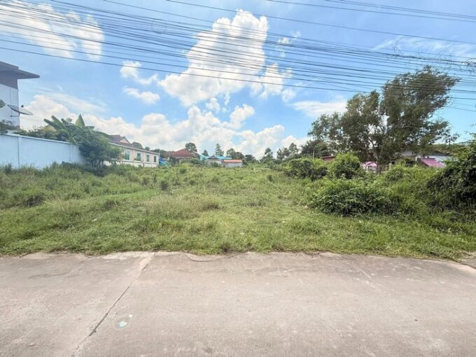 Wide view of a grassy vacant lot in a residential area with power lines overhead and houses in the background.