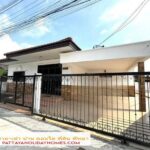 White single-story house behind a black wrought-iron gate with a long driveway, for sale in Pattaya.