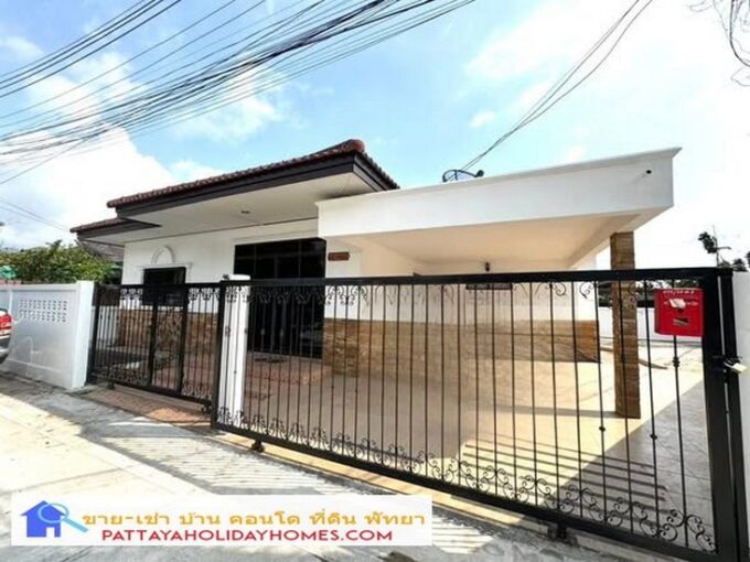 White single-story house behind a black wrought-iron gate with a long driveway, for sale in Pattaya.