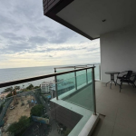 Baan Plai Haad Condo for Sale Balcony with glass railing overlooking the ocean, a high-rise building to the left, and a small round table with two chairs.