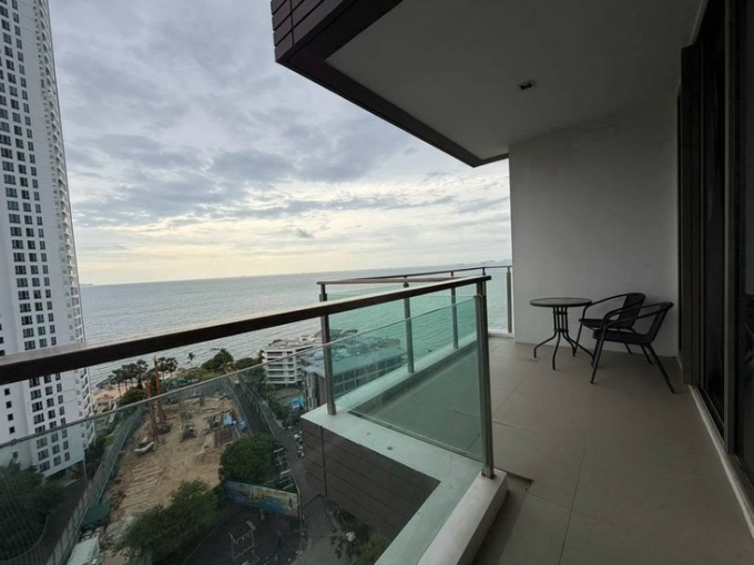 Baan Plai Haad Condo for Sale Balcony with glass railing overlooking the ocean, a high-rise building to the left, and a small round table with two chairs.
