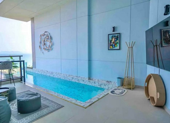 Indoor balcony pool on blue walls with mosaic edge, modern seating, and ocean view beyond the railing.